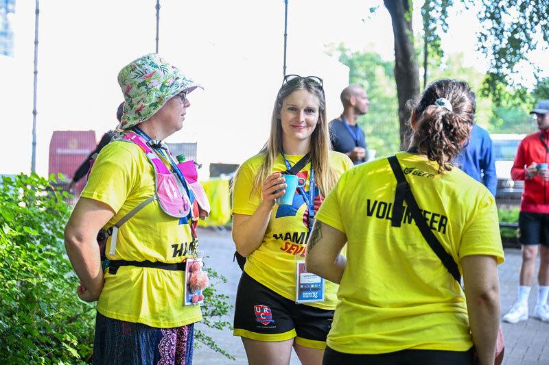 Drei Volunteers der Hamburg 7s stehen in gelben T-Shirts mit Volunteerschriftzug auf dem Rücken im Kreis zusammen