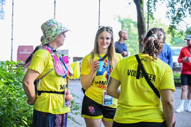 Drei Volunteers der Hamburg 7s stehen in gelben T-Shirts mit Volunteerschriftzug auf dem R&uuml;cken im Kreis zusammen