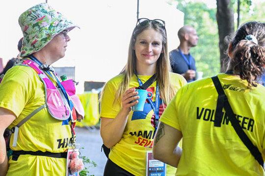 Drei Volunteers der Hamburg 7s stehen in gelben T-Shirts mit Volunteerschriftzug auf dem Rücken im Kreis zusammen