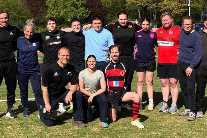 Eine Gruppe von 13 männlichen und weiblichen Trainern und Trainerinnen bei Sonneschein auf dem Kunstrasenplatz der Rugby-Arena Stadtpark